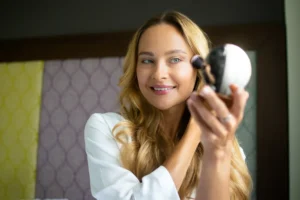 Nuori nainen katsoo peiliin ja levittää highlighteria poskipäilleen, hymyillen tyytyväisenä.